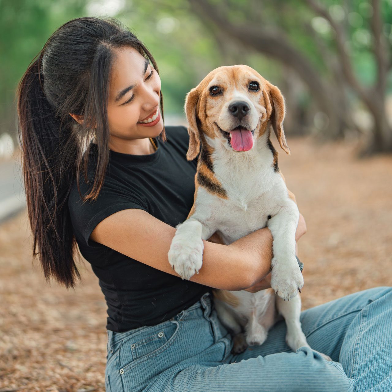 smiling young woman sitting in the park holding her dog